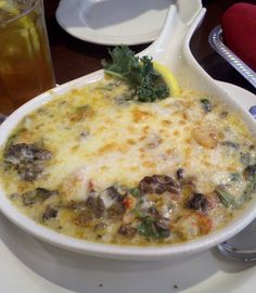 a white bowl filled with food on top of a plate next to a cup and spoon