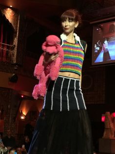 a woman holding a pink teddy bear on top of a runway