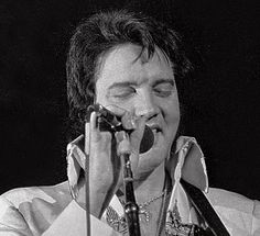 elvis presley singing into a microphone while holding his hands up to his face in front of him