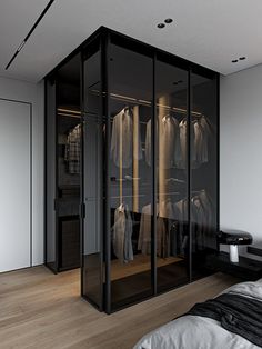 a walk in closet with glass doors and clothes hanging on hangers next to a bed