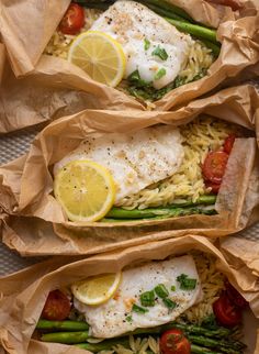 three fish and asparagus wrapped in brown paper with lemon wedges on top