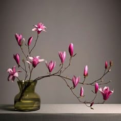 a green vase with pink flowers in it on a white countertop against a gray background