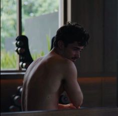 a shirtless man sitting in a bathtub looking at his reflection on the mirror