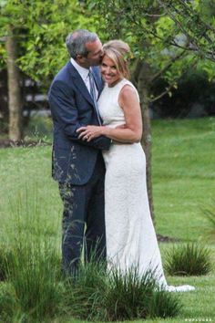 a man and woman standing next to each other in front of a tree with their arms around each other