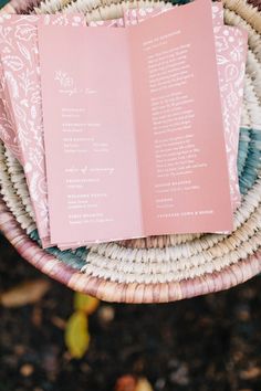 two pink wedding programs sitting on top of a wicker basket next to each other