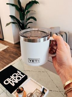 a person holding up a yeti cup in front of a table with other items on it