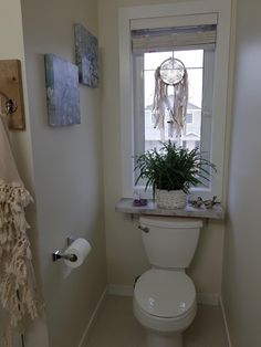 a white toilet sitting in a bathroom next to a window with a dream catcher on it