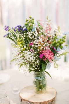 a vase filled with lots of flowers sitting on top of a wooden table next to glasses