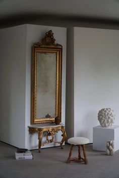 a room with a mirror, stool and sculpture on the floor in front of it