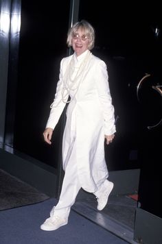 an older woman in white is walking down the street with her hand on her hip