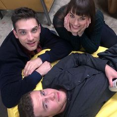 two men and a woman laying on the floor with their arms around each other, smiling