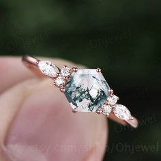 a woman's hand holding an engagement ring with a green and white stone in the middle