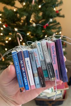 a hand holding a bunch of books in front of a christmas tree