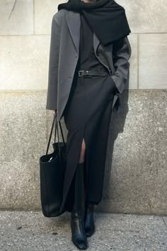 a woman standing next to a wall holding a black bag and wearing a gray coat