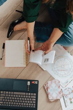 a woman is sitting on the floor with her laptop and notebook in front of her