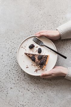 a person holding a plate with a slice of pie on it and two blackberries