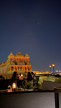 two people are sitting on a bench in front of an ornate building at night time