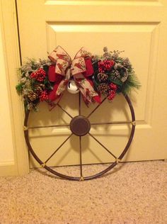 a wagon wheel decorated with pine cones, berries and holly wreaths is sitting in front of a door