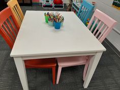 a white table with four chairs and a blue cup filled with pencils on it