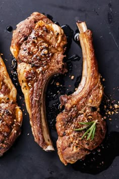 two pieces of meat sitting on top of a black surface with spices and seasoning