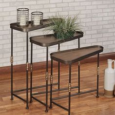 three metal tables with plants on them in front of a brick wall and wooden floor