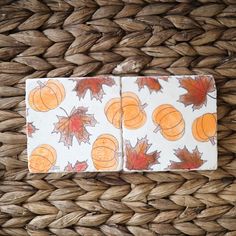 two napkins with autumn leaves and pumpkins on them sitting on a woven basket