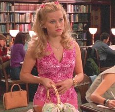 a woman in a pink dress holding a basket and sitting at a table with other people