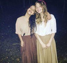 two young women standing next to each other in the woods at night, with their arms around each other