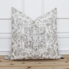 a white and grey pillow sitting on top of a wooden floor next to a wall