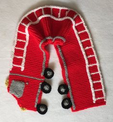 a red knitted scarf with black buttons and white trim on the bottom is laying on a white surface