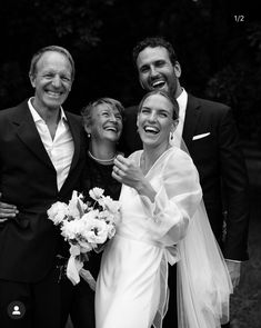 a group of people standing next to each other in front of trees and bushes smiling at the camera