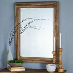 a mirror sitting on top of a wooden table next to a vase and candle holder