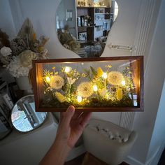 a person holding up a glass case with flowers in it and lights on the inside