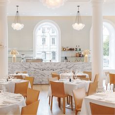 an image of a restaurant setting with white tables and orange chairs in front of the counter