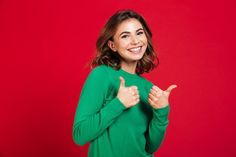 a woman in a green shirt is giving the thumbs up sign with both hands on a red background