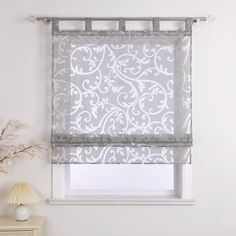 a window with a gray and white roman blind in front of the window, next to a dresser