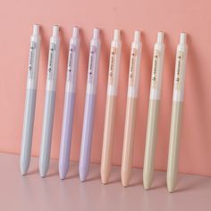 five different colored pens lined up against a pink wall with writing on the top and bottom