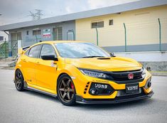 a yellow honda civic type car parked in front of a building on the side of the road