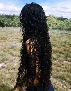 the back of a woman's head with long curly hair sitting in a field