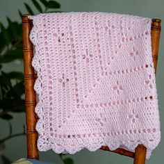 a pink crocheted blanket sitting on top of a wooden chair next to a plant