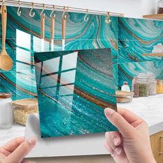 two hands holding up a photo in front of a kitchen counter with blue marble tiles