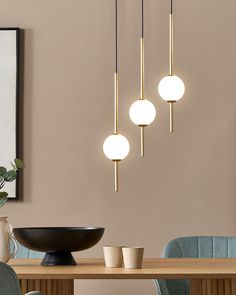 three lights hanging from the ceiling above a table with two chairs and a bowl on it