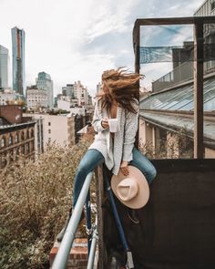 a woman sitting on top of a building with her hair blowing in the wind and holding a coffee cup