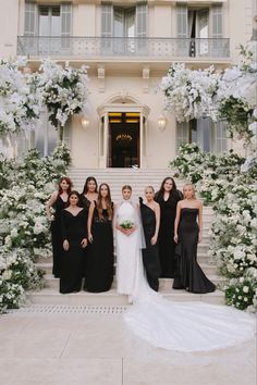 a group of people standing in front of a building with white flowers and greenery