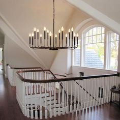 a chandelier hanging from the ceiling in a room with hardwood floors and white railings