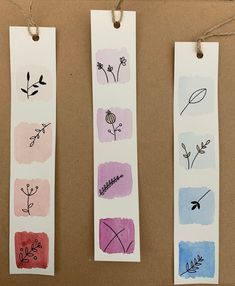 three bookmarks with flowers and leaves on them hanging from twine strings in front of a brown background