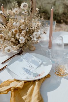 the table is set with white plates and silverware, candles, and flowers in vases