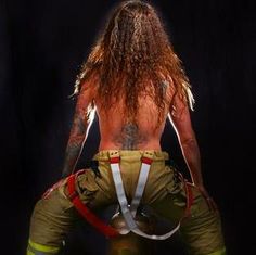 a man with long hair and tattoos on his back is wearing fireman's pants