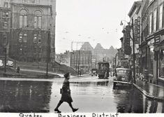 an old black and white photo of a woman walking down the street in the rain