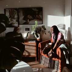 a woman sitting on top of an orange chair in a living room next to a plant